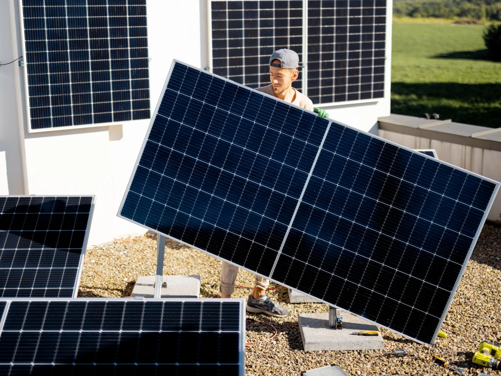 Muž nese solární panel při instalaci solární elektrárny na střeše nemovitosti.